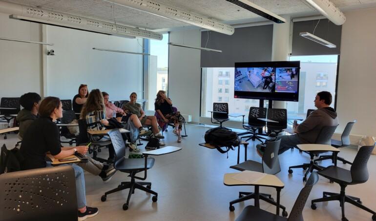 Opiskelijoita luokassa seuraamassa simulaatiota televisioruudulta.
